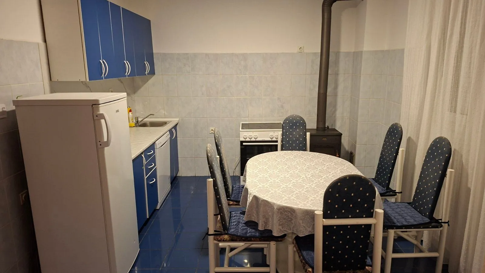 Kuhinja sa plavim elementima i trpezarijskim stolom sa stolicama.