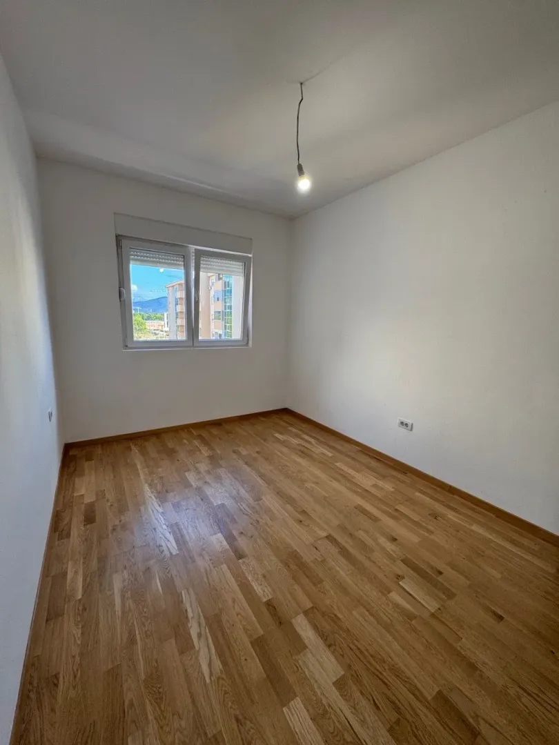 Prazna soba sa drvenim parketom i bijelim zidovima.