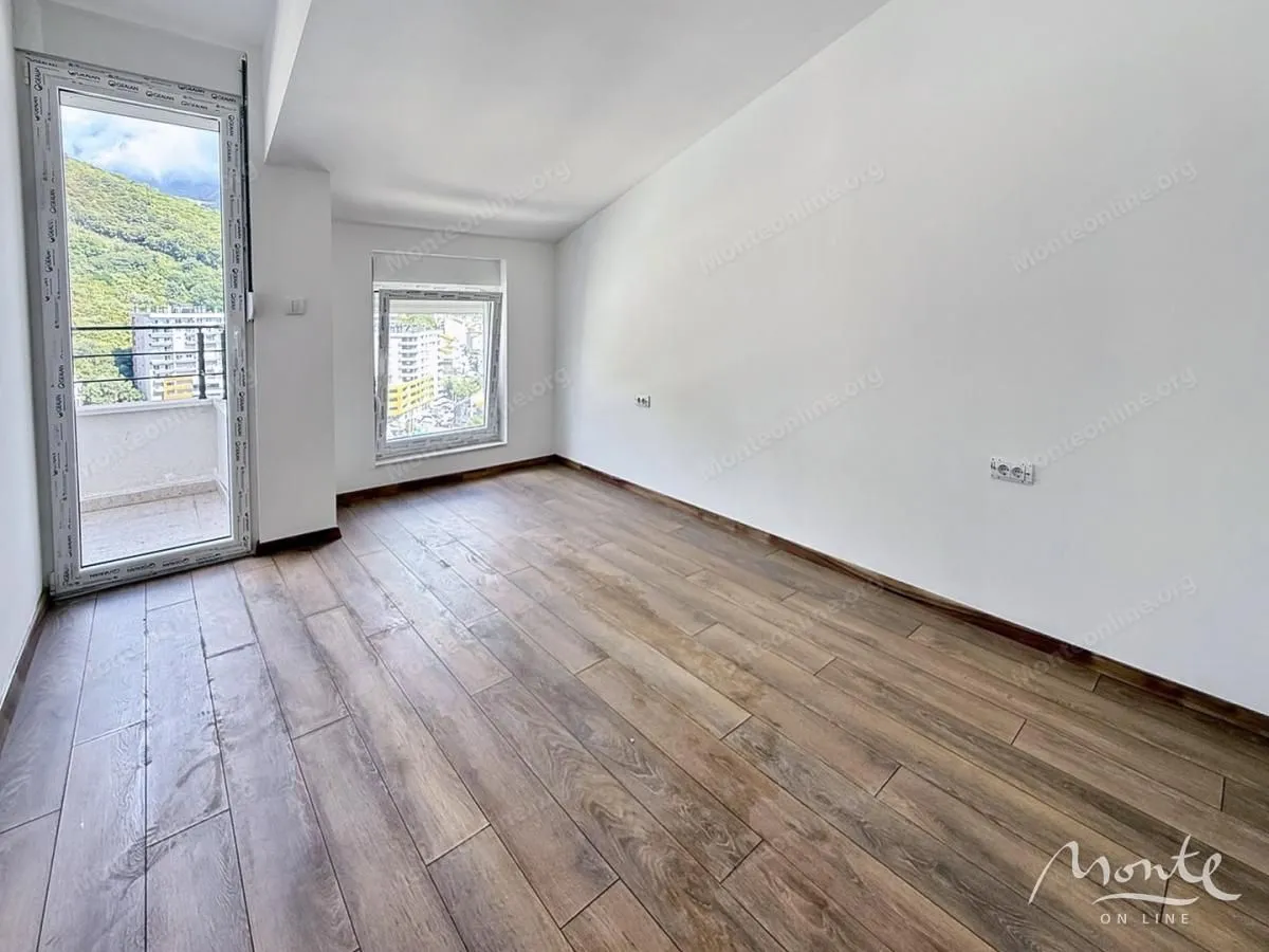 Prazna soba sa drvenim podom, bijelim zidovima i izlazom na balkon.