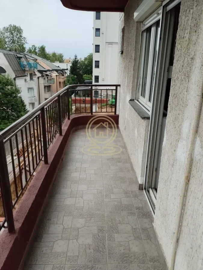 Dugi popločani balkon sa metalnom ogradom i pogledom na okolne zgrade.