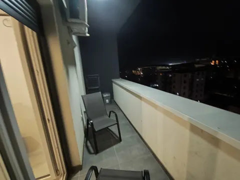 Osvetljena terasa sa stolicama i pogledom na grad noću. - image 12