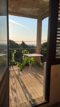 View through the open door onto a balcony with a table and a view of greenery and the sea. - image 8