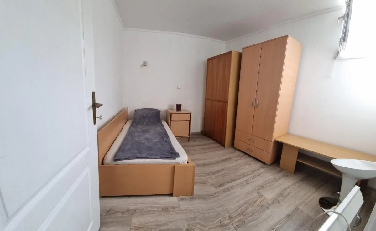 Manja spavaća soba sa krevetom, ormarima i laminatom na podu.