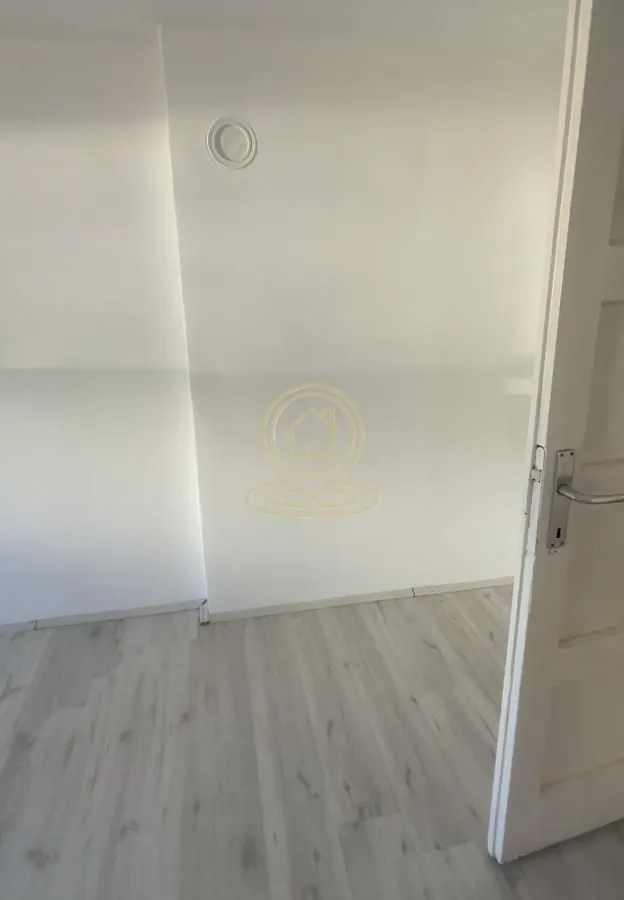 Prazna prostorija sa belim zidovima i svetlim laminatom.