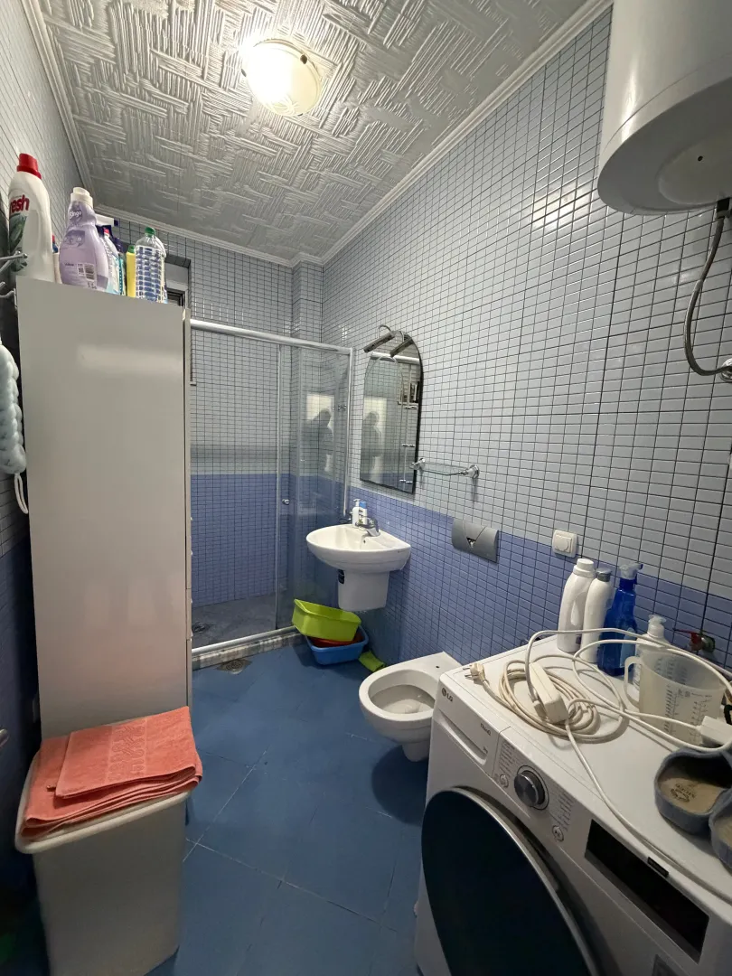 Manje kupatilo sa plavim pločicama, tuš kabinom i veš mašinom.