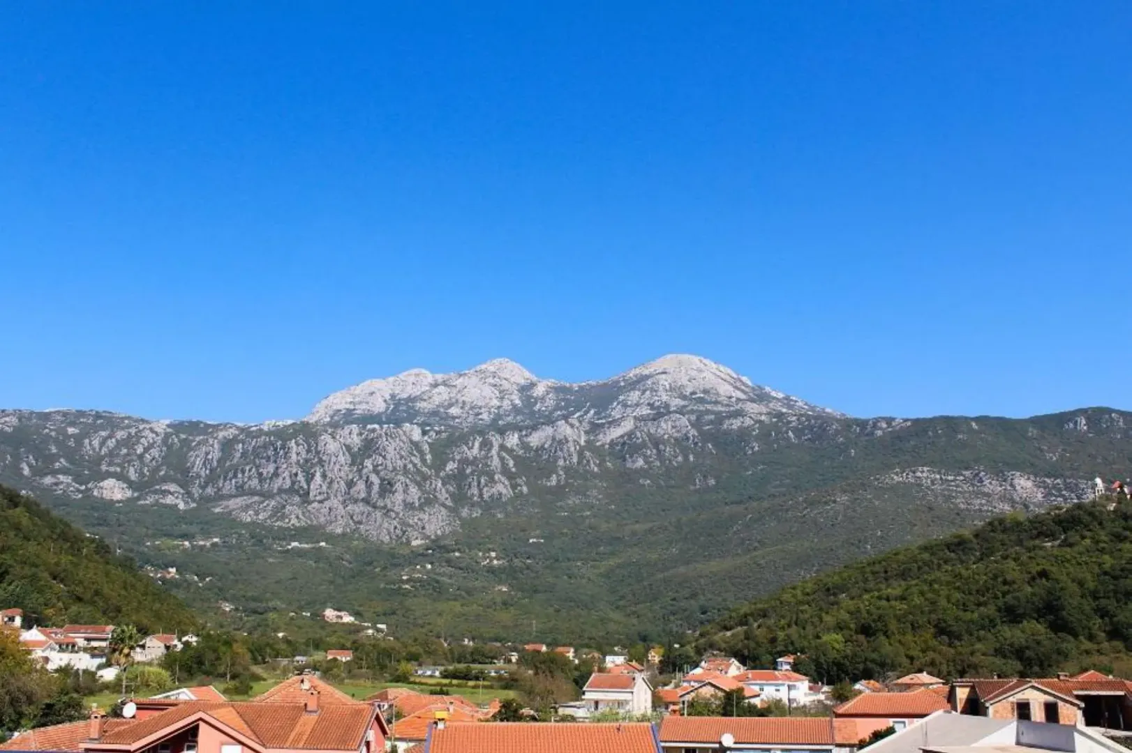 Pogled na planinu i okolno naselje sa krovovima kuća u prvom planu.