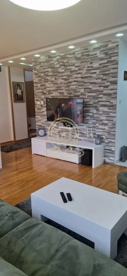 Dnevna soba sa garniturom, TV-om i belim komadom nameštaja.