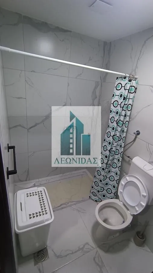 Bathroom lined with marble tiles featuring a toilet and a shower cabin with a curtain.