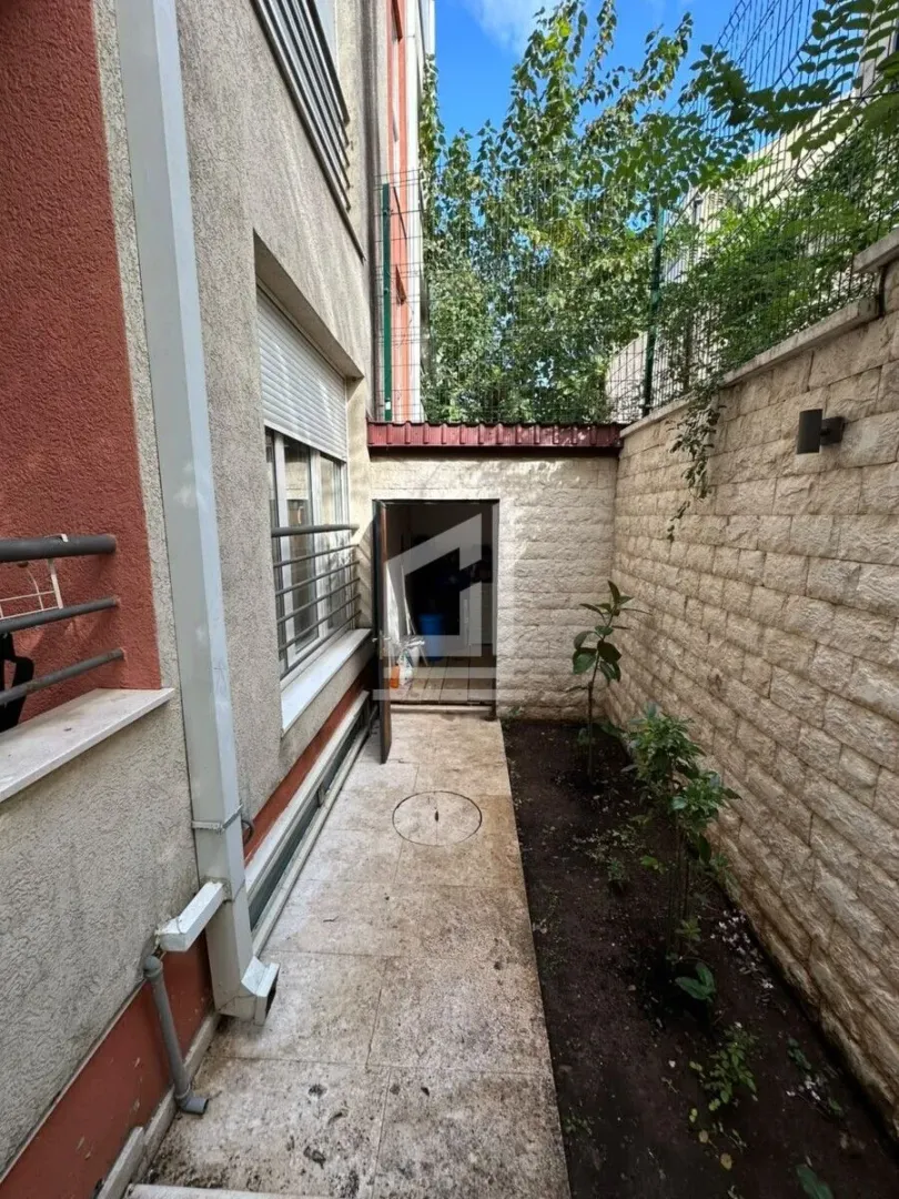 Manje dvorište pored zgrade sa popločanim stazama i malom baštom.