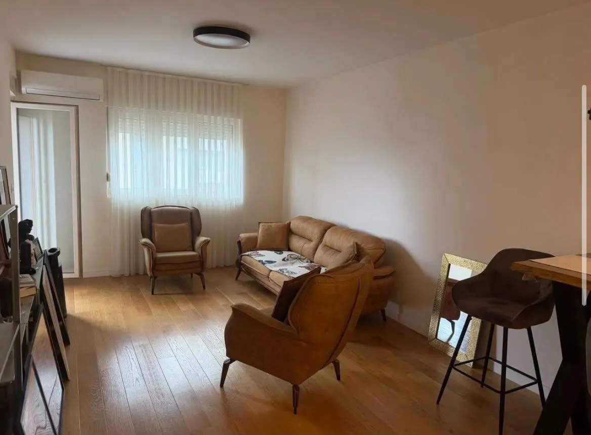 Dnevna soba sa garniturom za sedenje, foteljama i drvenim podom.