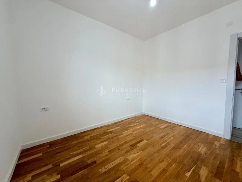 Prazna soba sa drvenim parketom i bijelim zidovima.