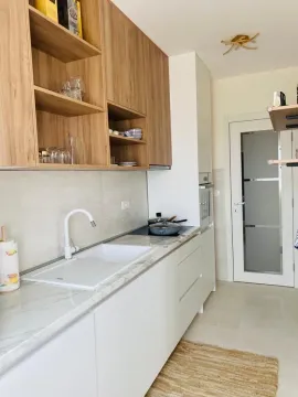 Svijetla moderna kuhinja sa drvenim visećim elementima i bijelom radnom površinom. - image 9