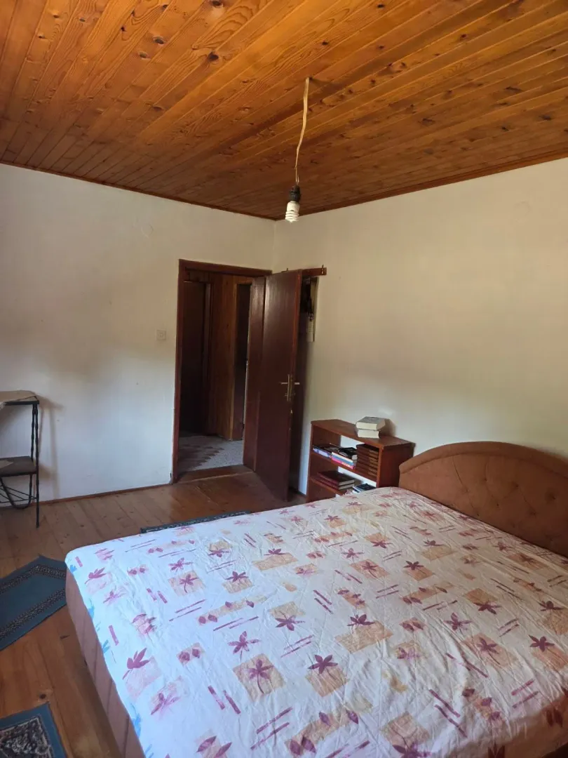 Spavaća soba sa bračnim krevetom, drvenim plafonom i vratima koja vode u hodnik.