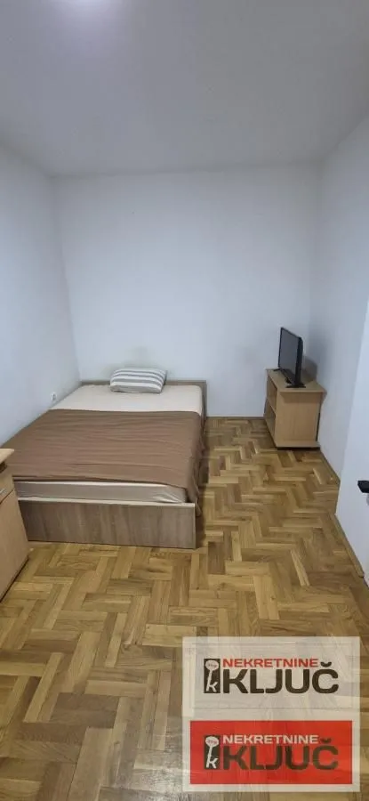 Nameštena spavaća soba sa bračnim krevetom i parketom.