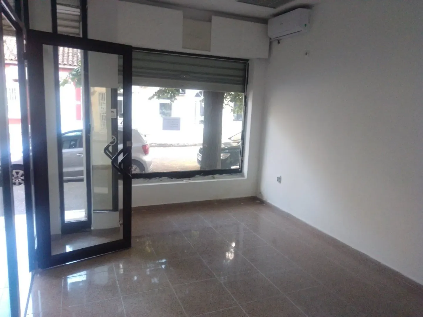 Empty commercial space with glass entrance doors and tiled flooring.