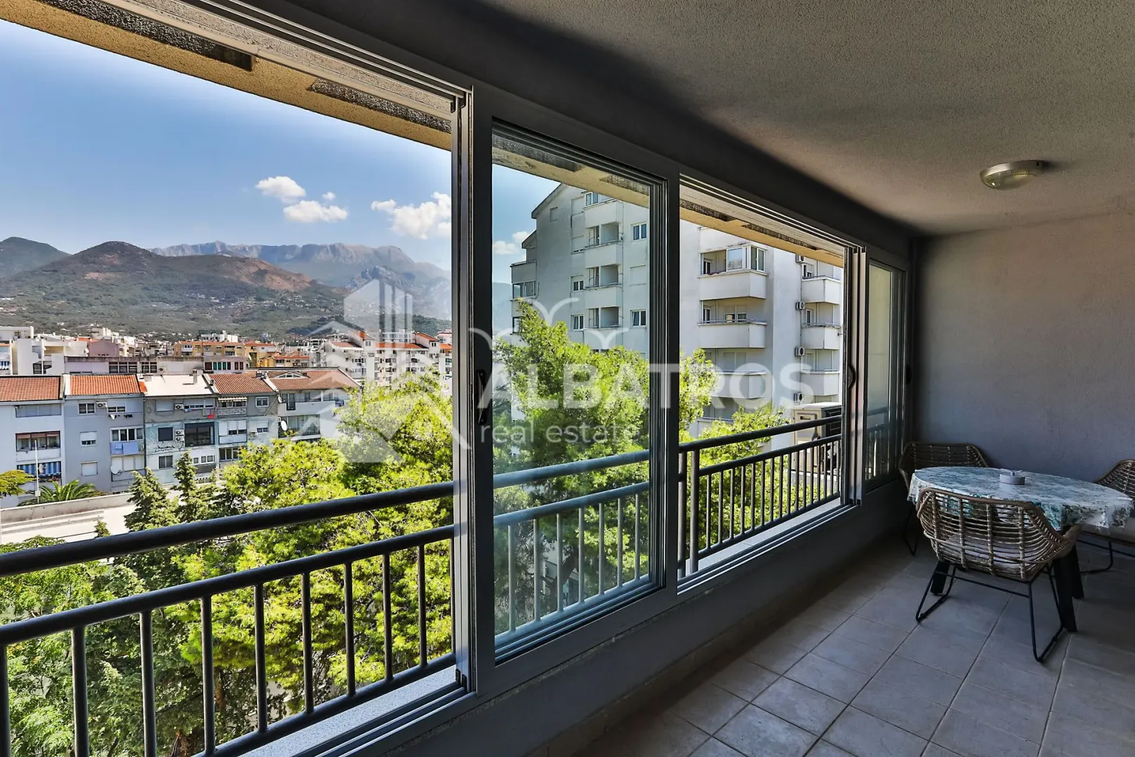 Zastakljeni balkon sa garniturom za sjedenje i pogledom na grad.