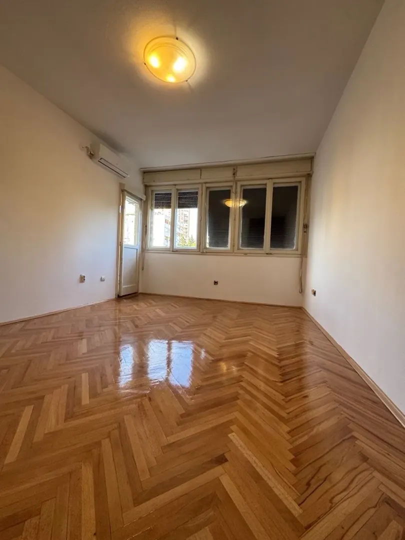 Empty room with parquet flooring and windows.