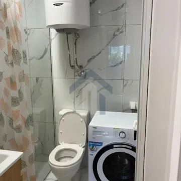 Manje kupatilo sa bijelim pločicama, toaletom i veš mašinom. - image 9