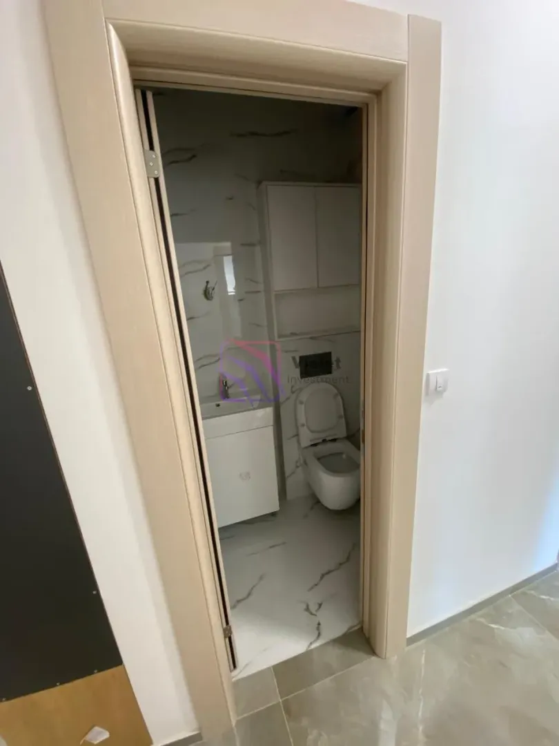 Pogled iz hodnika na manje kupatilo sa sanitarijama i bijelim ormarićem.