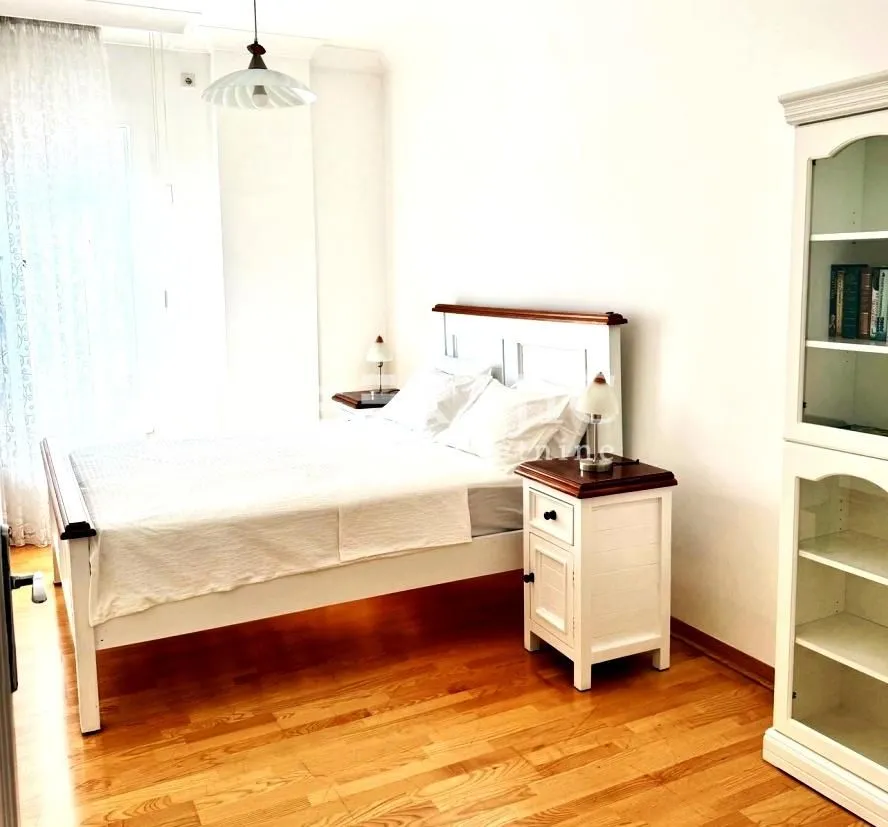 Bright bedroom with a double bed, nightstand, and a white display cabinet.
