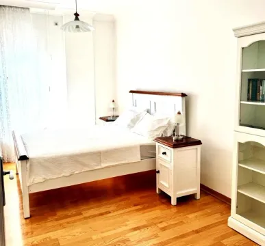 Bright bedroom with a double bed, nightstand, and a white display cabinet. - image 3