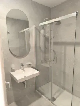 Moderne kupatilo sa tuš kabinom, umivaonikom i ovalnim ogledalom obloženo sivim pločicama. - image 5