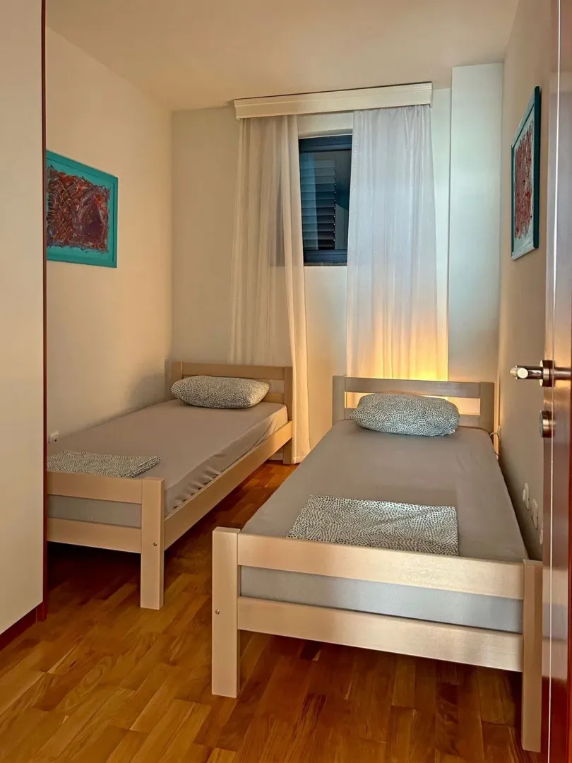Spavaća soba sa dva odvojena kreveta i drvenim podom.