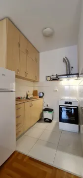 Mala kuhinja sa svijetlim drvenim elementima, šporetom i frižiderom. - image 4
