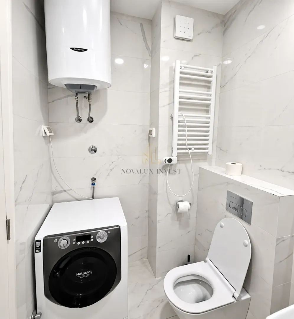 Kupatilo sa wc šoljom, veš mašinom i bojlerom na zidu.