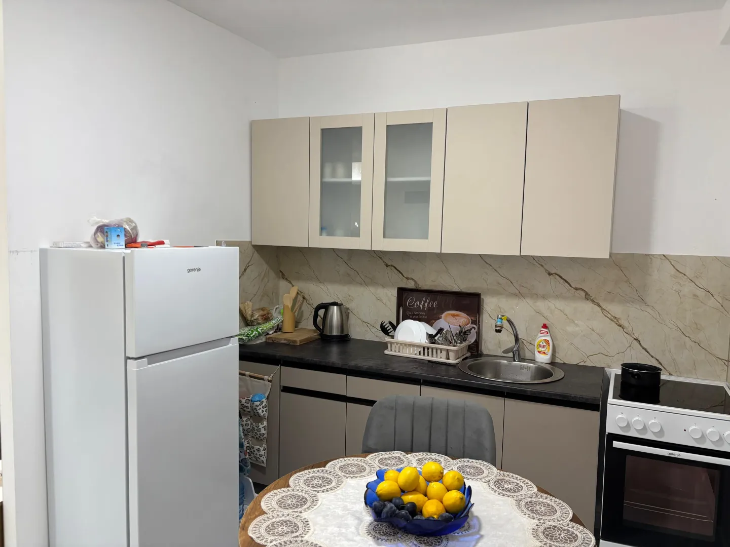 Manja kuhinja sa trpezarijskim stolom, frižiderom i elementima u bež tonovima.