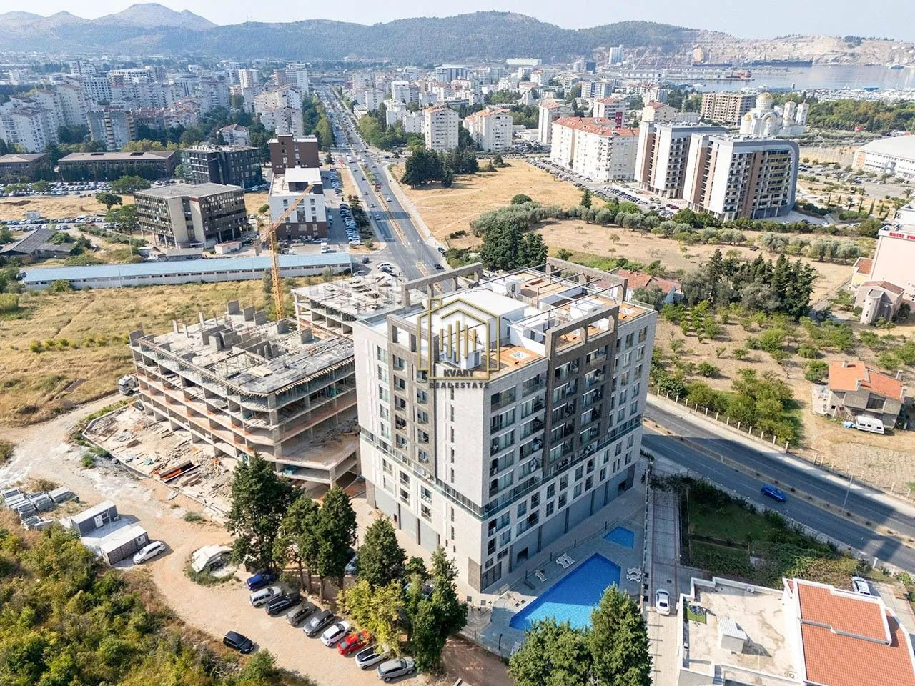 Aerial view of the residential building and surrounding neighborhood with a swimming pool and parking.