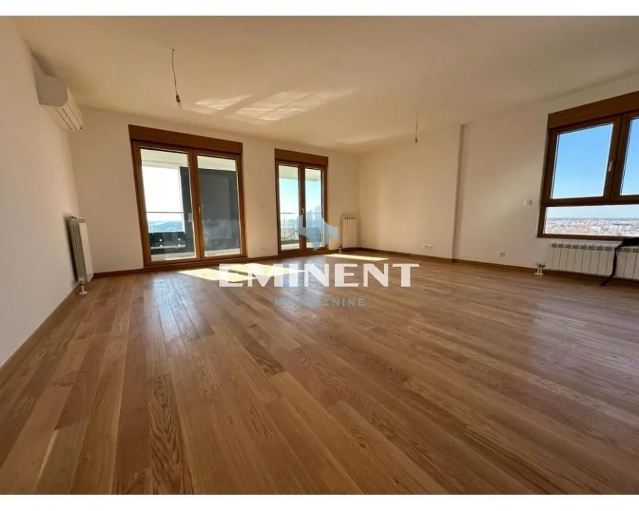 Spacious empty room with wooden flooring and large windows leading to the terrace.
