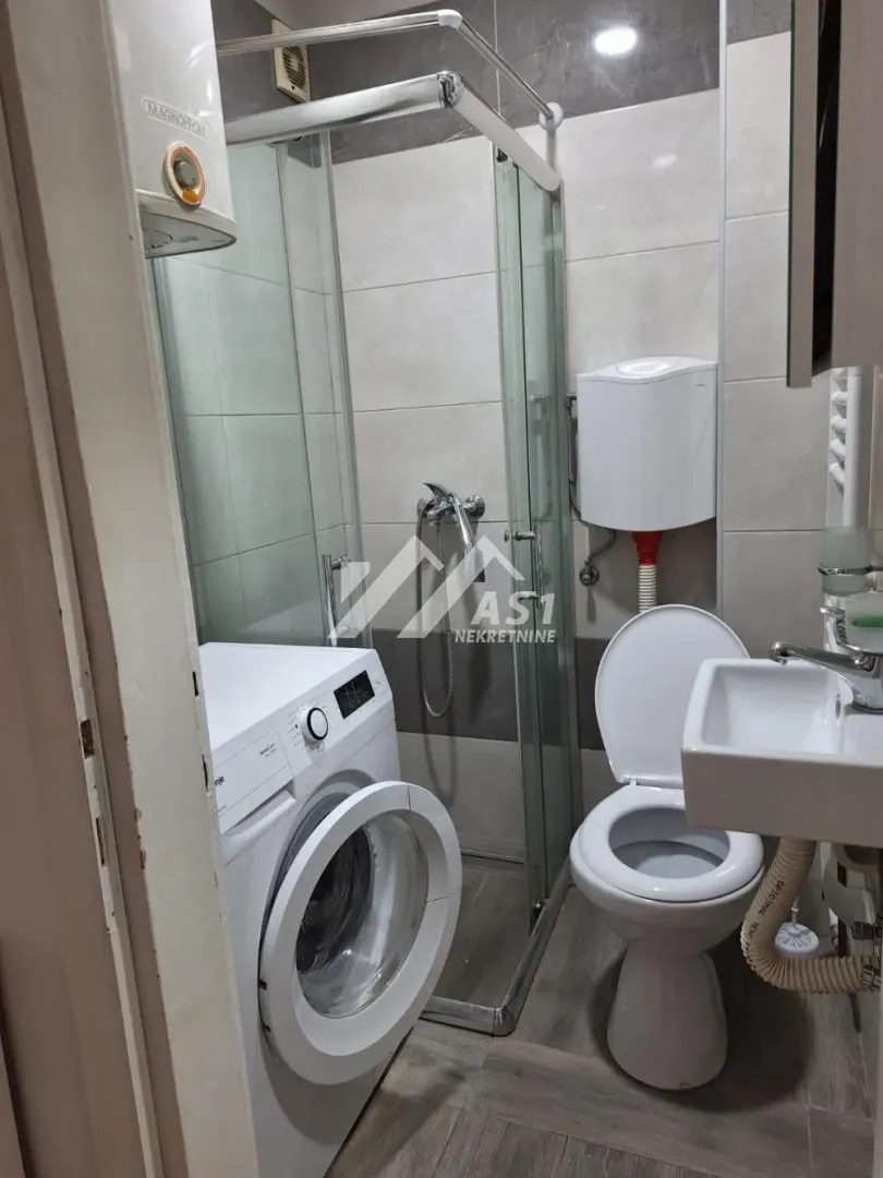 Manje kupatilo sa tuš kabinom, WC šoljom, umivaonikom i mašinom za veš.