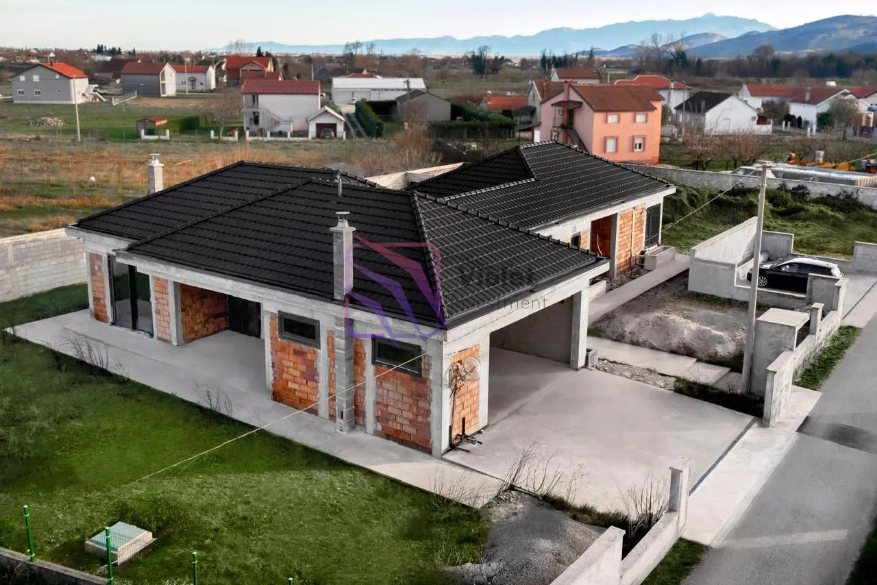 Pogled iz vazduha na prizemnu kuću u izgradnji sa crnim krovom i dvorištem.