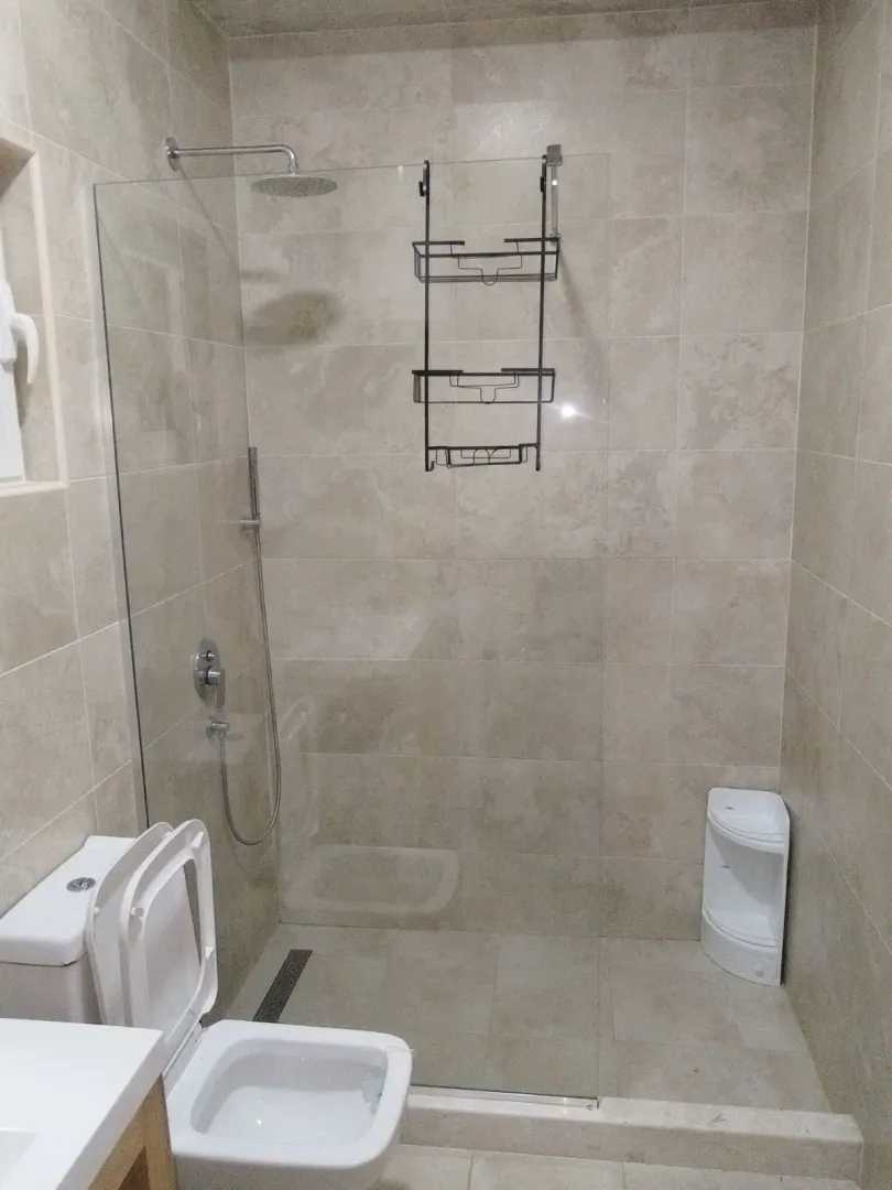Moderno opremljeno kupatilo sa tuš kabinom obloženom pločicama u bež tonovima.