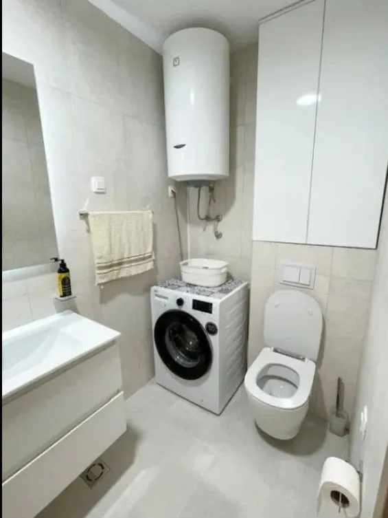 Compact bathroom with a sink, toilet, washing machine, and water heater.