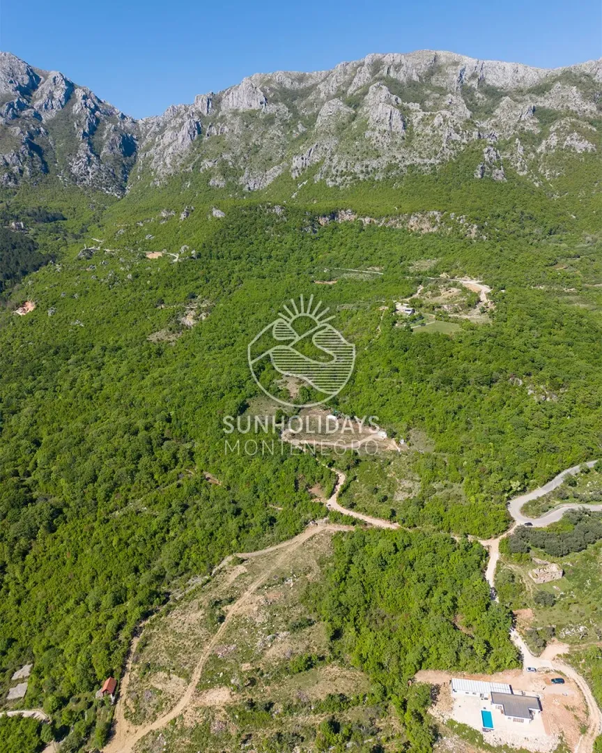 Pogled iz vazduha na planinski krajolik sa šumom i objektom u prirodi.