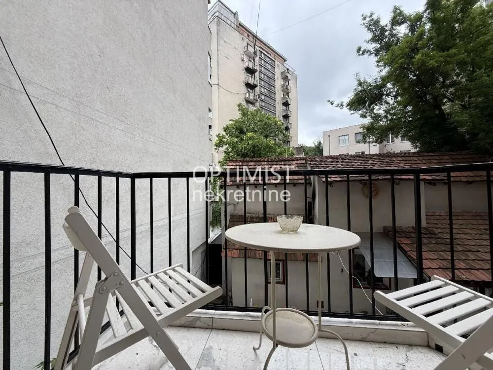 Small furnished balcony with a table and chairs and a view of surrounding buildings.