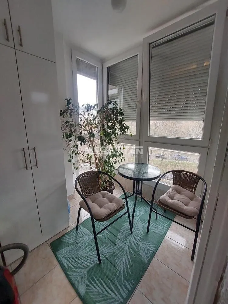 Zastakljeni balkon sa malim stolom, dve stolice i ugrađenim ormarom.