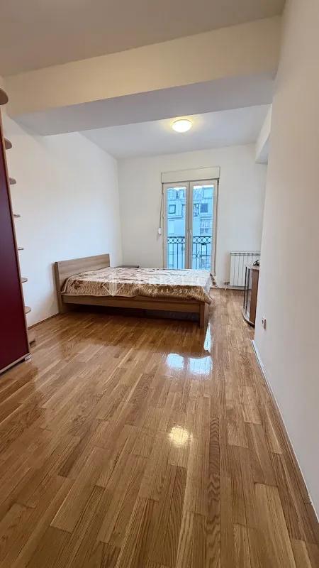 Spavaća soba sa bračnim krevetom, drvenim parketom i izlazom na terasu.