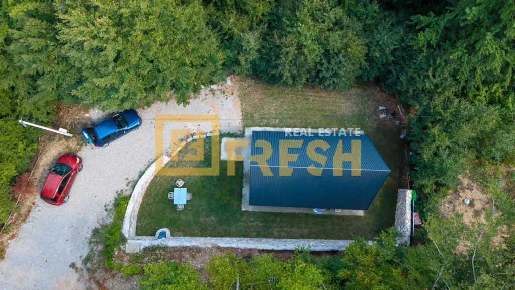 Pogled iz vazduha na imanje sa kućom i dvorištem okruženim šumom.