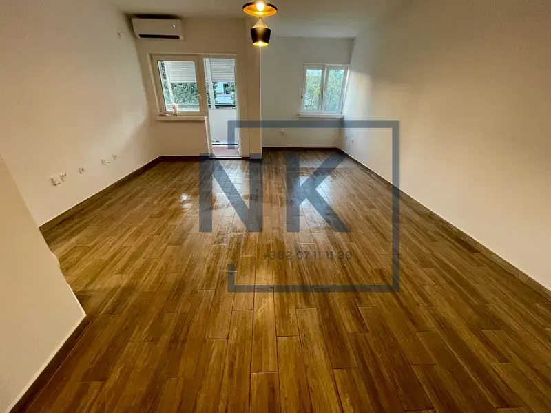 Empty room with wooden flooring and windows.