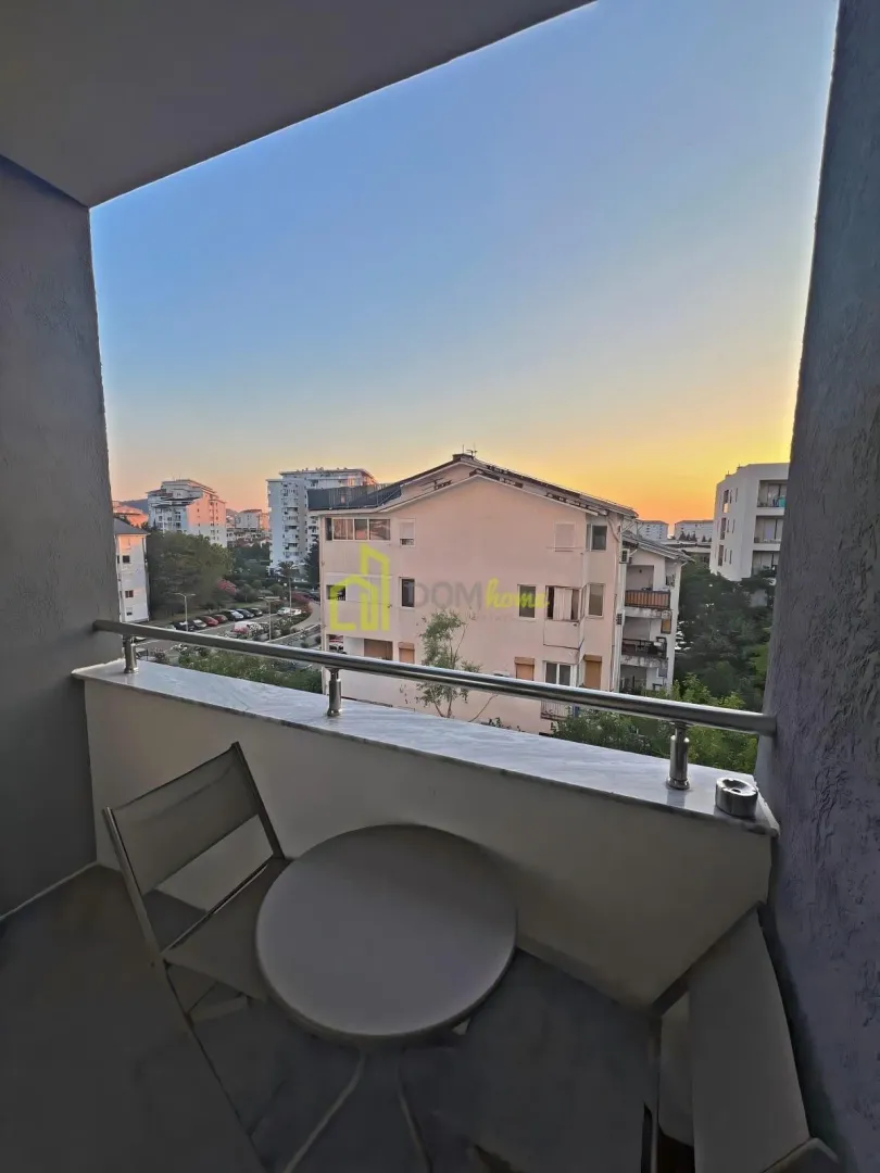 Small furnished balcony with a table and two chairs and a view of the surrounding buildings.