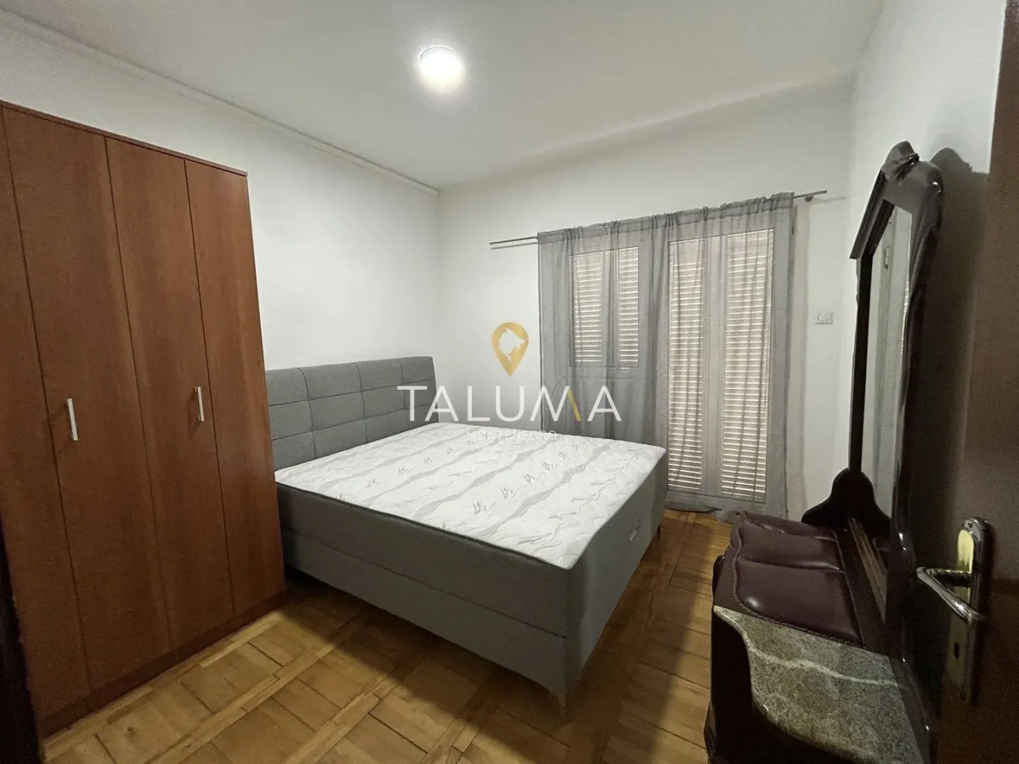 Furnished bedroom with a double bed, wooden wardrobe, and dresser with a mirror.