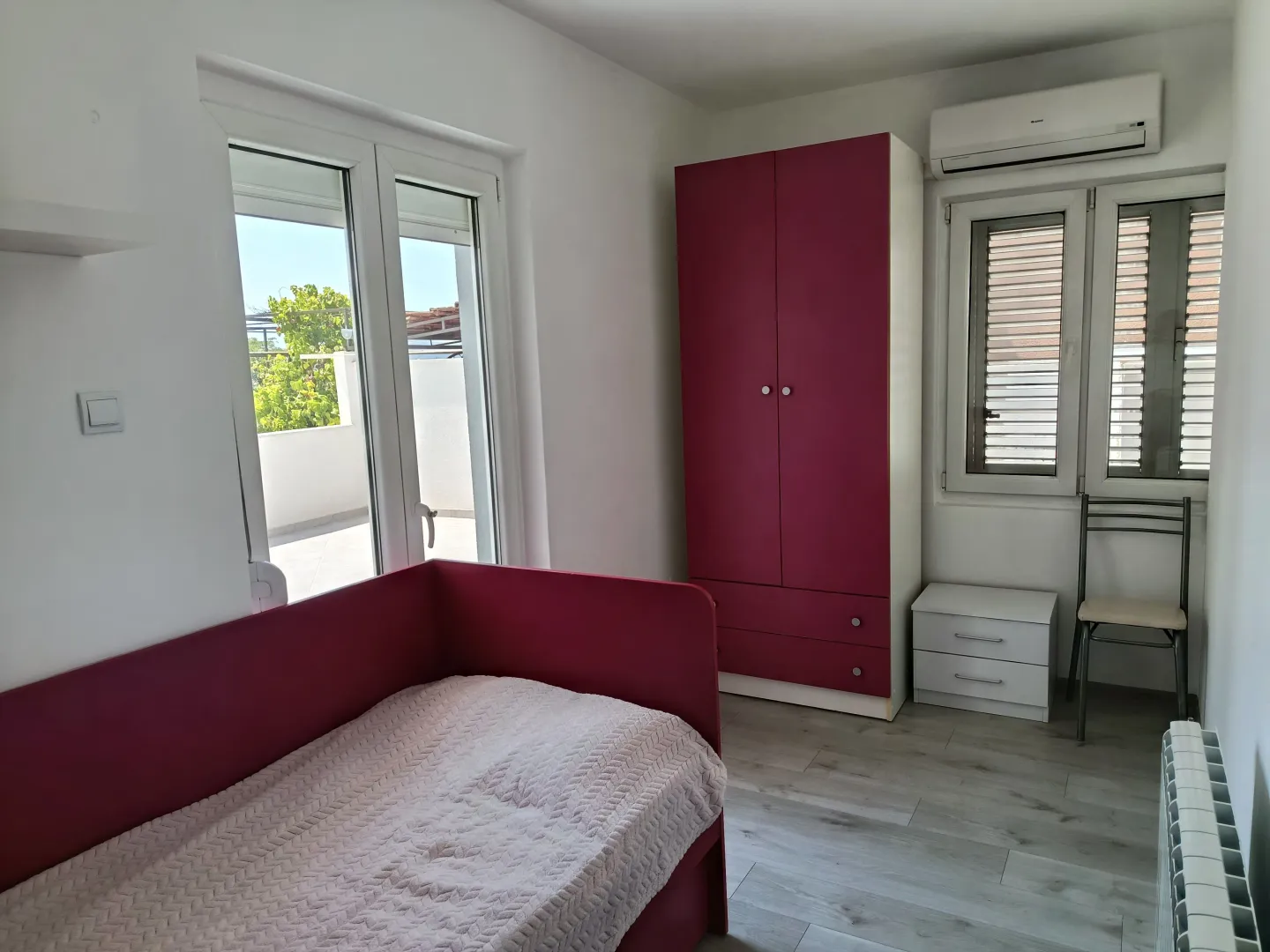 Namještena dječja soba sa krevetom, garderoberom i izlazom na terasu.