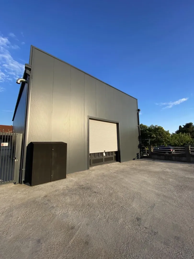 Exterior of a modern utility building with a roller shutter door and paved driveway.