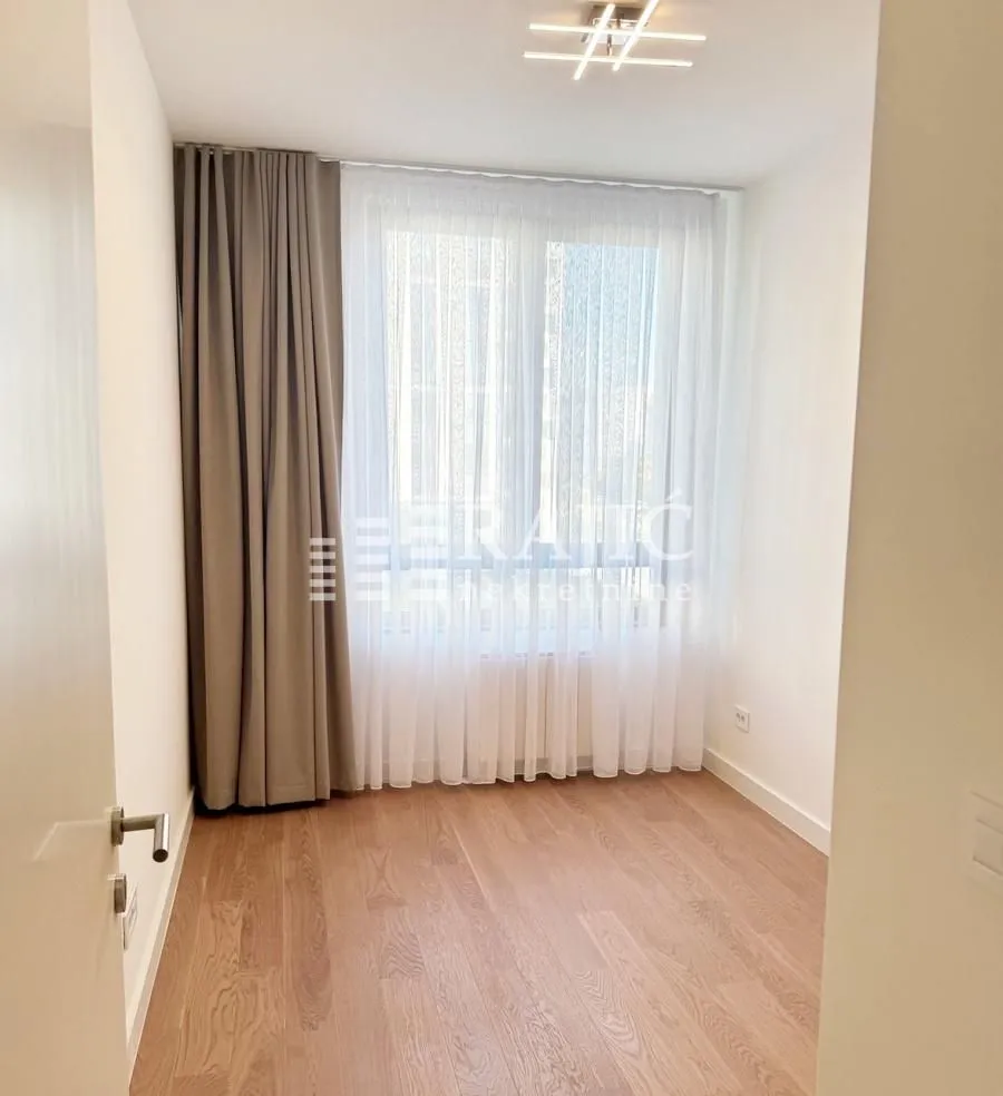 Empty room with wooden flooring, a large window, and curtains.