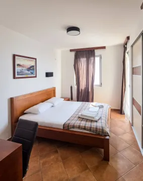 Spavaća soba sa bračnim krevetom, drvenim namještajem i prozorom sa zavjesama. - image 3