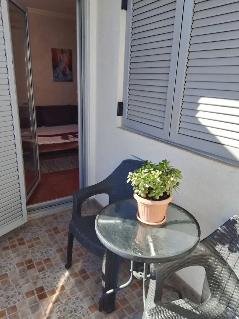 Manji namješteni balkon sa stolom, stolicama i saksijom cvijeća.