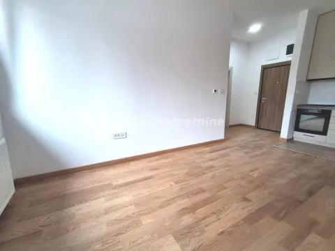 Empty room with wooden flooring and a partial view of the kitchen in the corner. - image 4